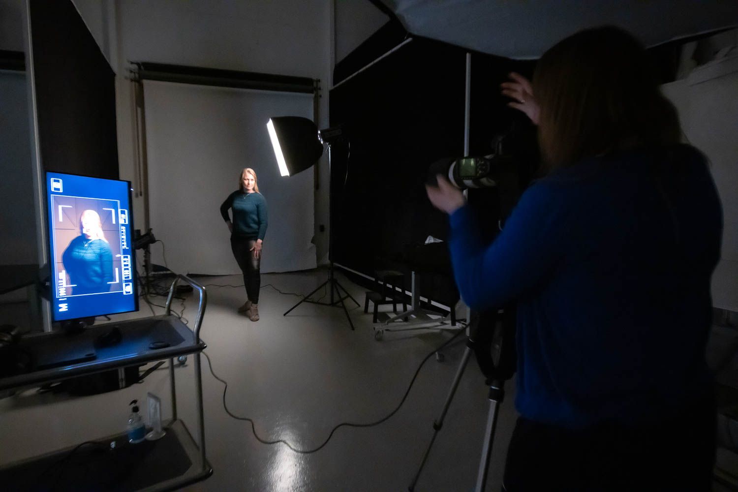Dark studio environment with professional lighting equipment and monitors visible during photo shoot.