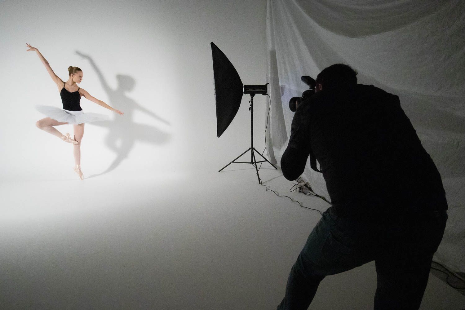 Silhouette of photographer capturing a ballet dancer against white backdrop.