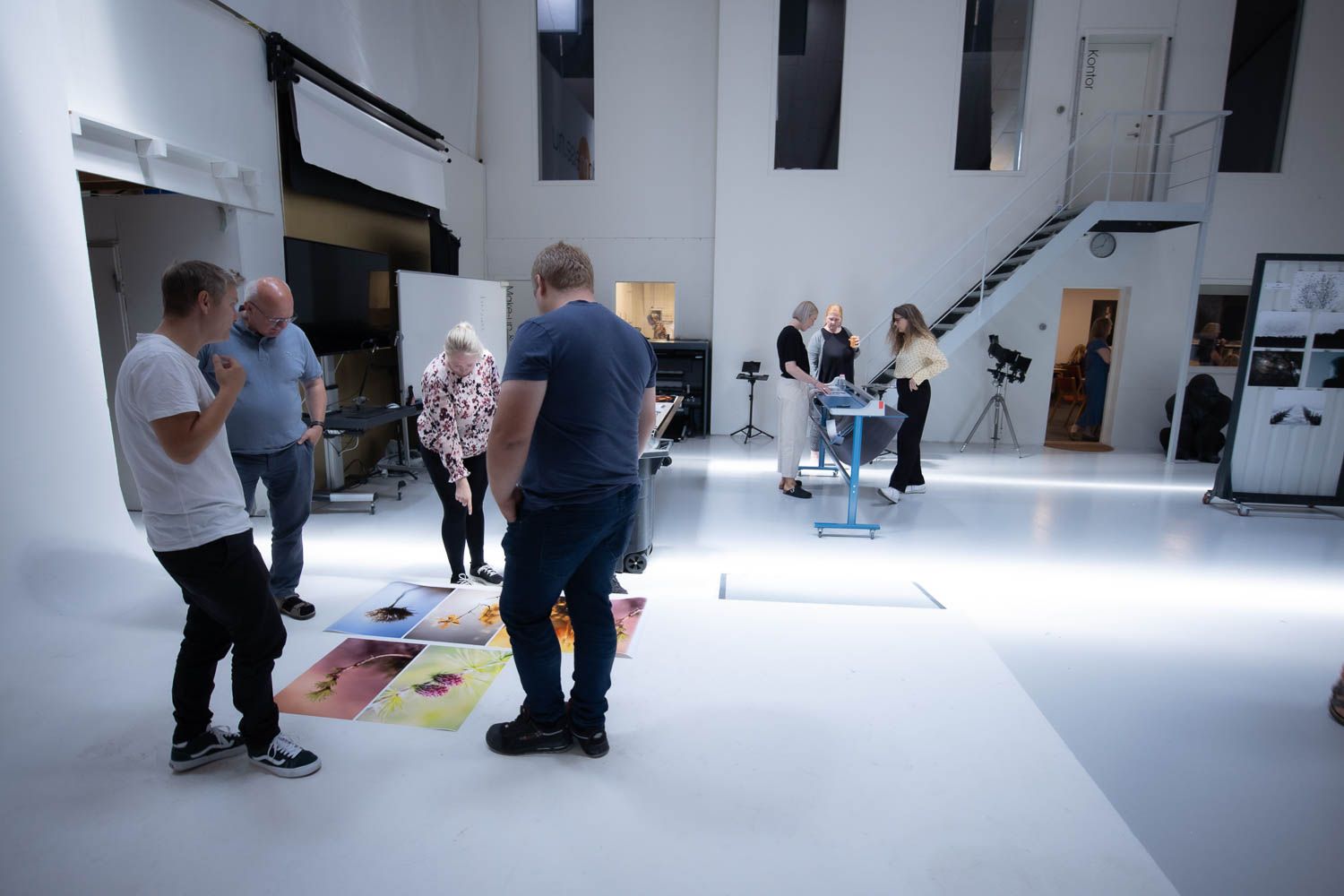 Group of people gathered in a bright white photography studio space reviewing materials.