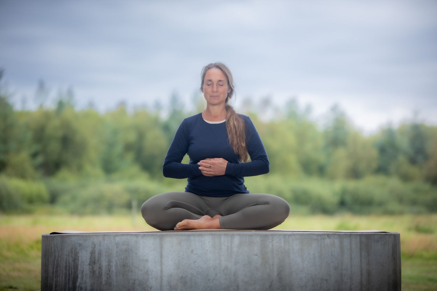 Person practicing meditation in lotus position on outdoor concrete platform.