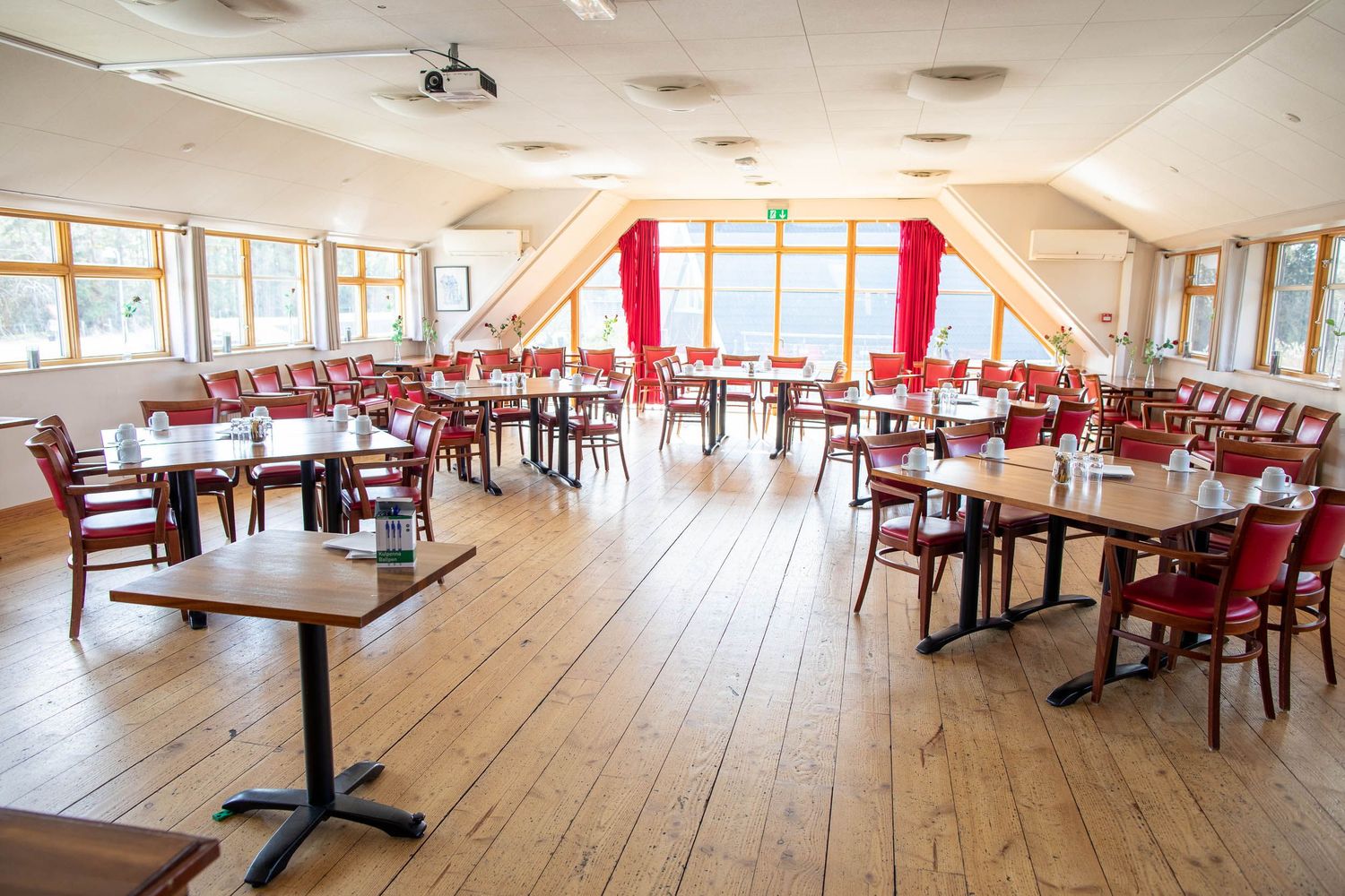 Modern restaurant dining room with red chairs and wooden floors bathed in natural light.