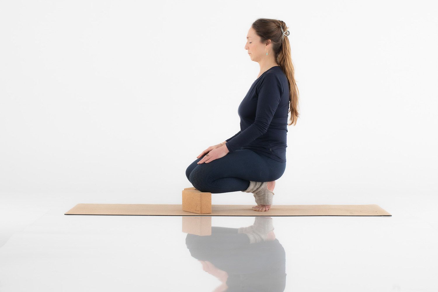 Person in navy outfit demonstrating yoga poses on a wooden platform against white background.