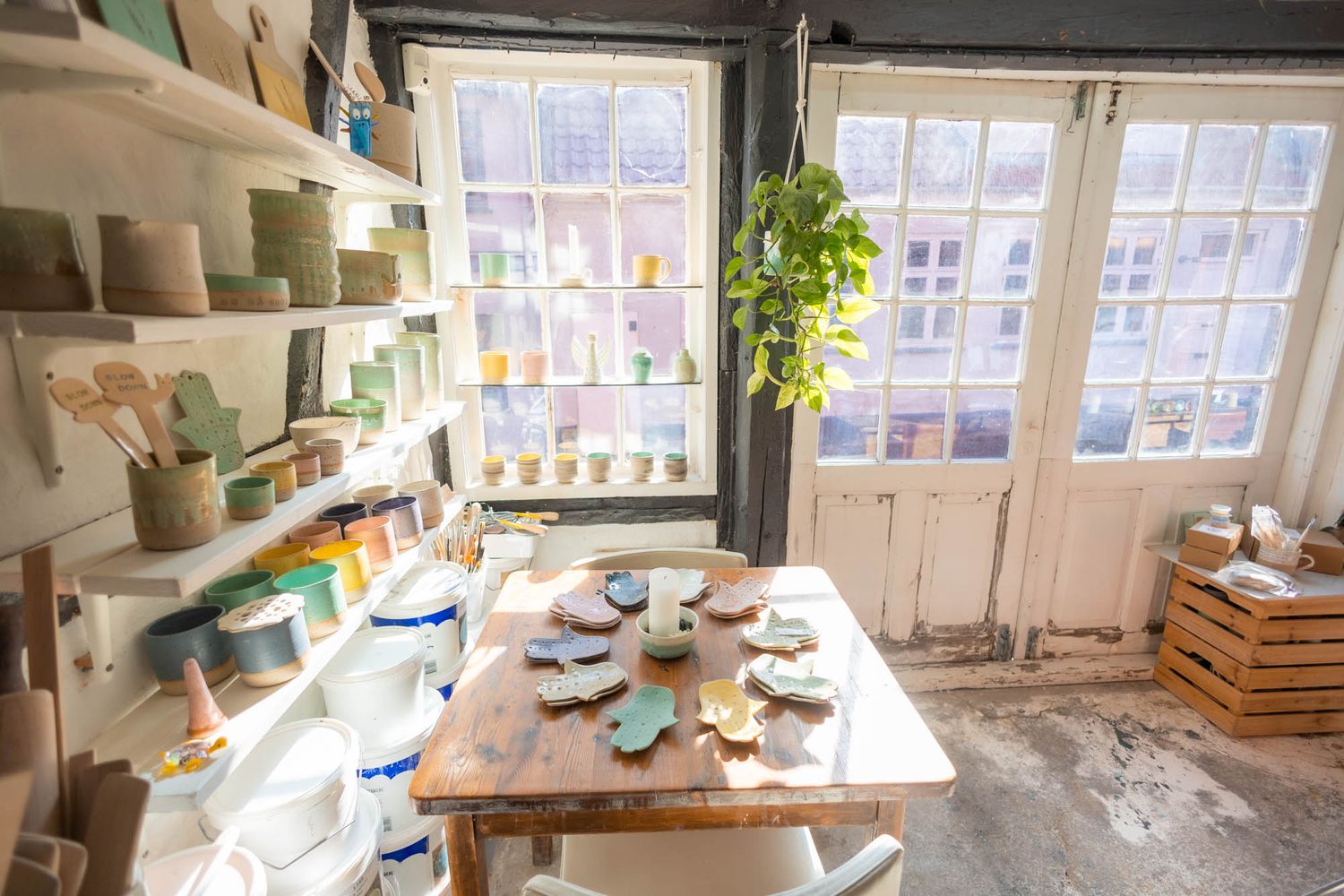 Pottery workshop space with shelves of ceramics and natural light streaming through windows.