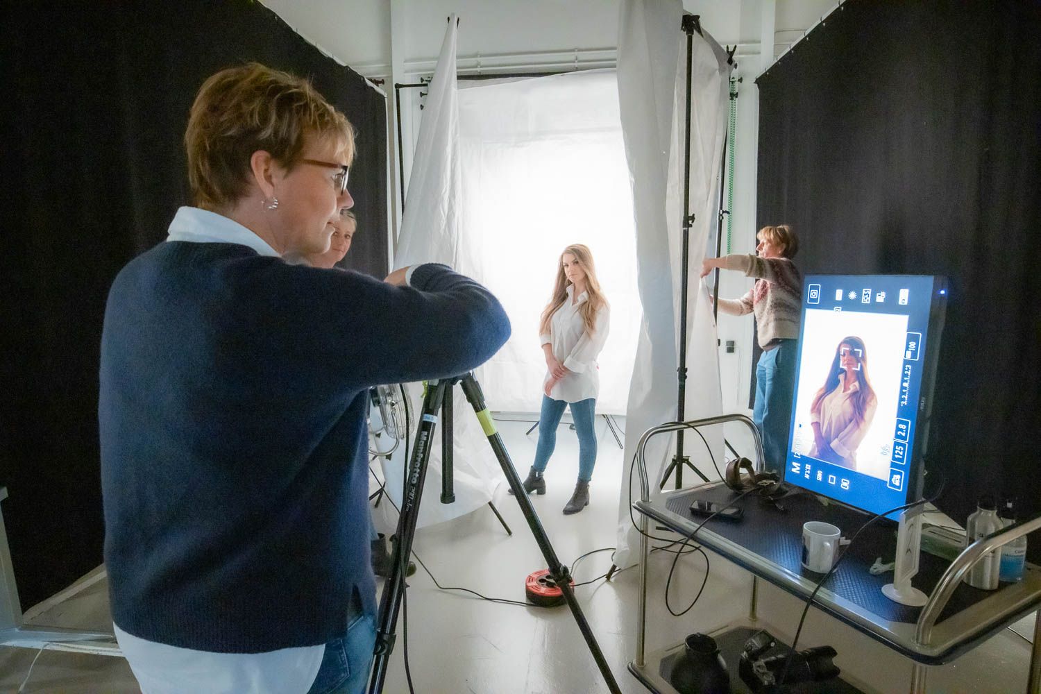 Behind the scenes view of a photo studio with lighting equipment and digital displays.