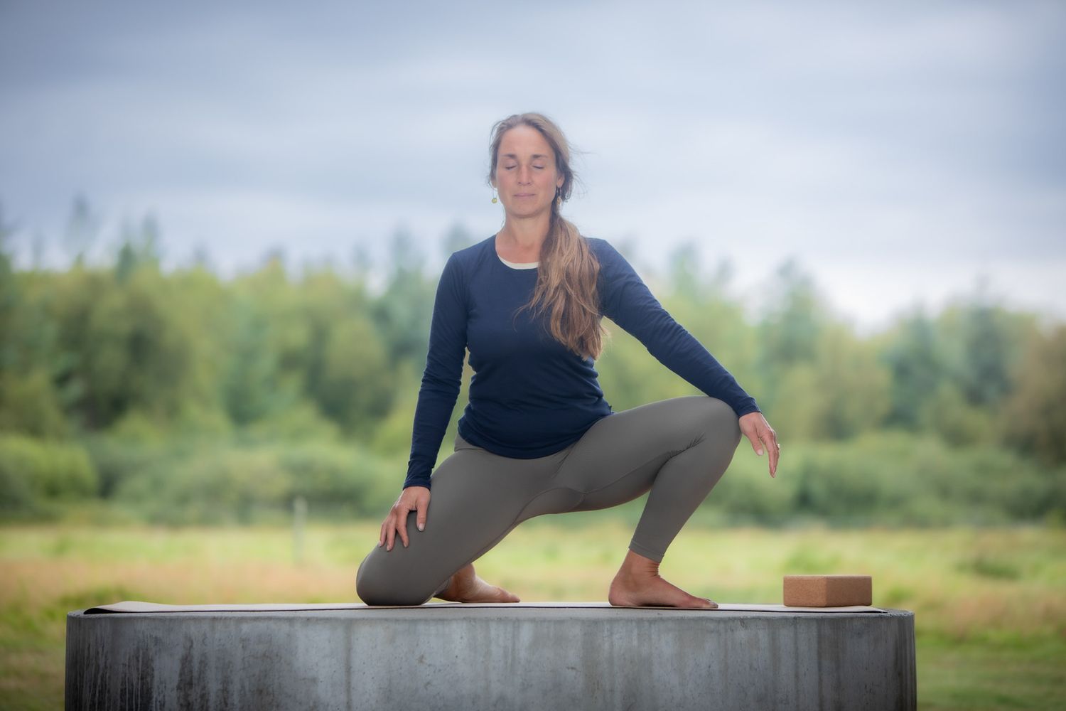 Person demonstrating yoga poses on concrete surface in grassy field.