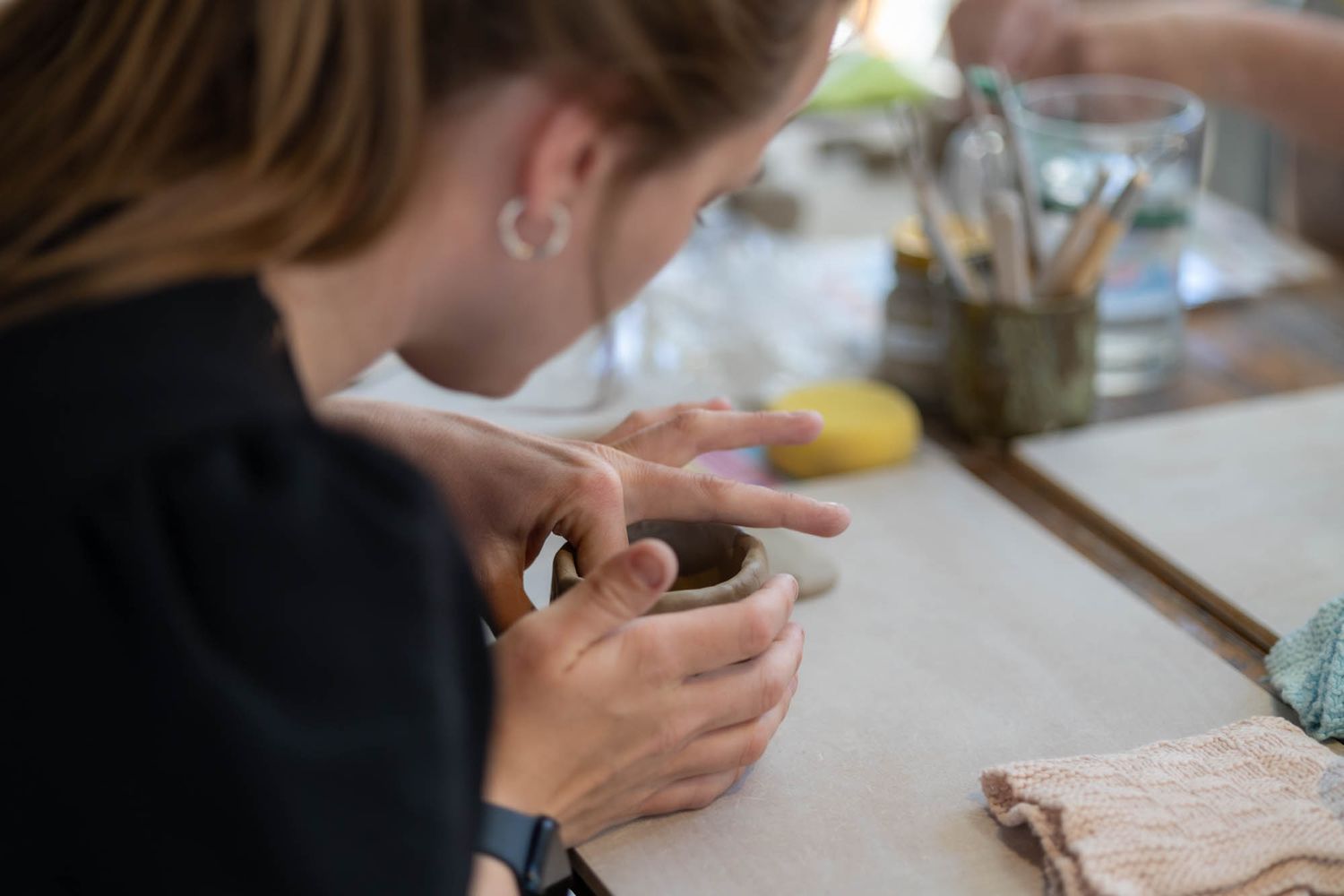 Close-up of hands working with clay and pottery tools on a work surface.