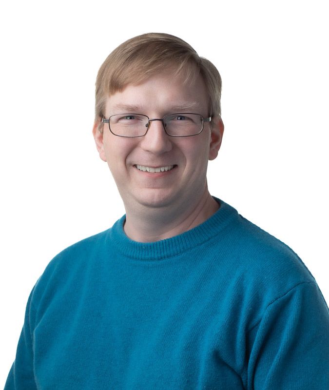 Person wearing glasses and a teal sweater shown in a professional headshot series against white background.