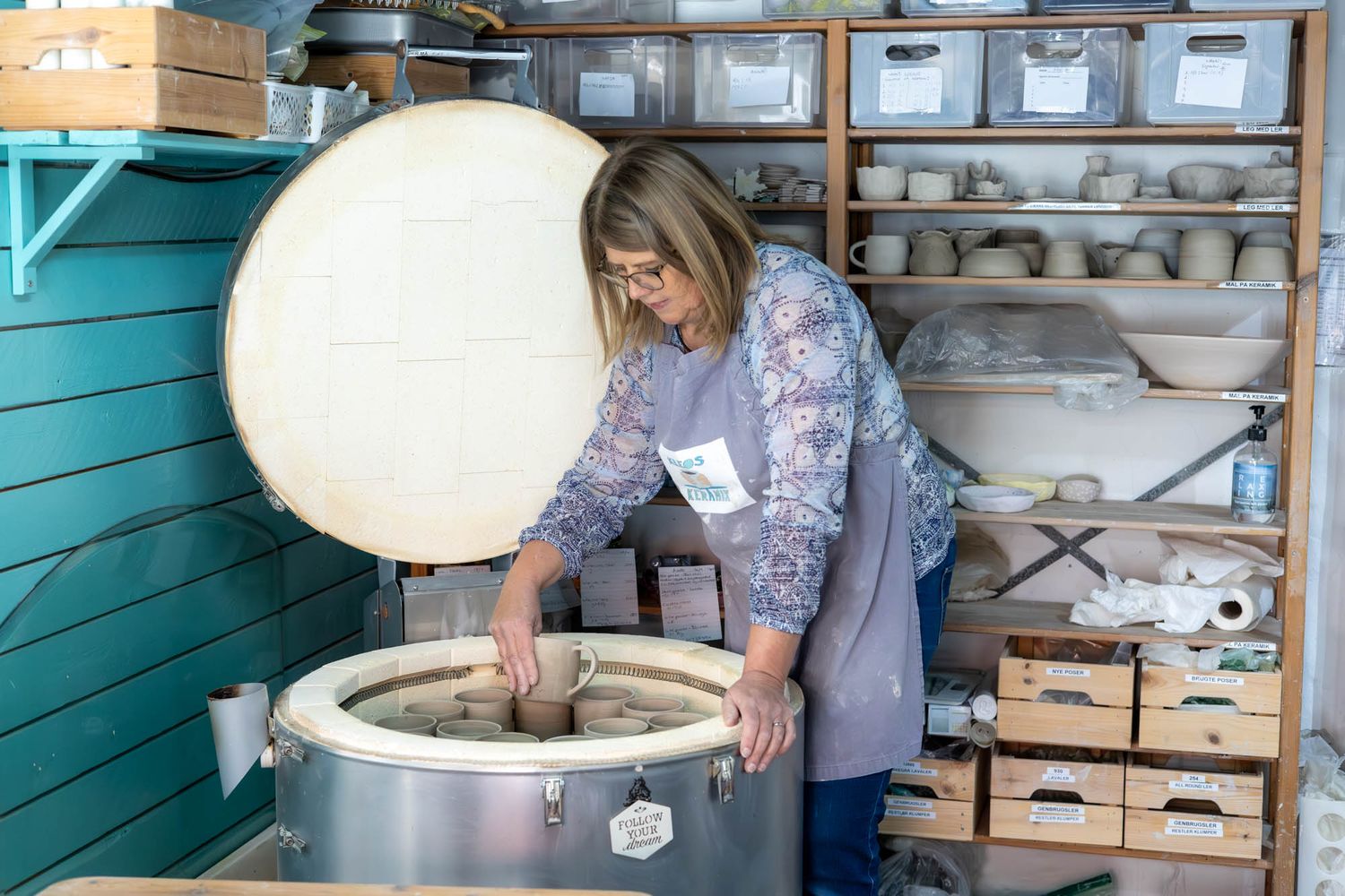 Artist opening a large kiln filled with ceramic pieces in a studio workspace.