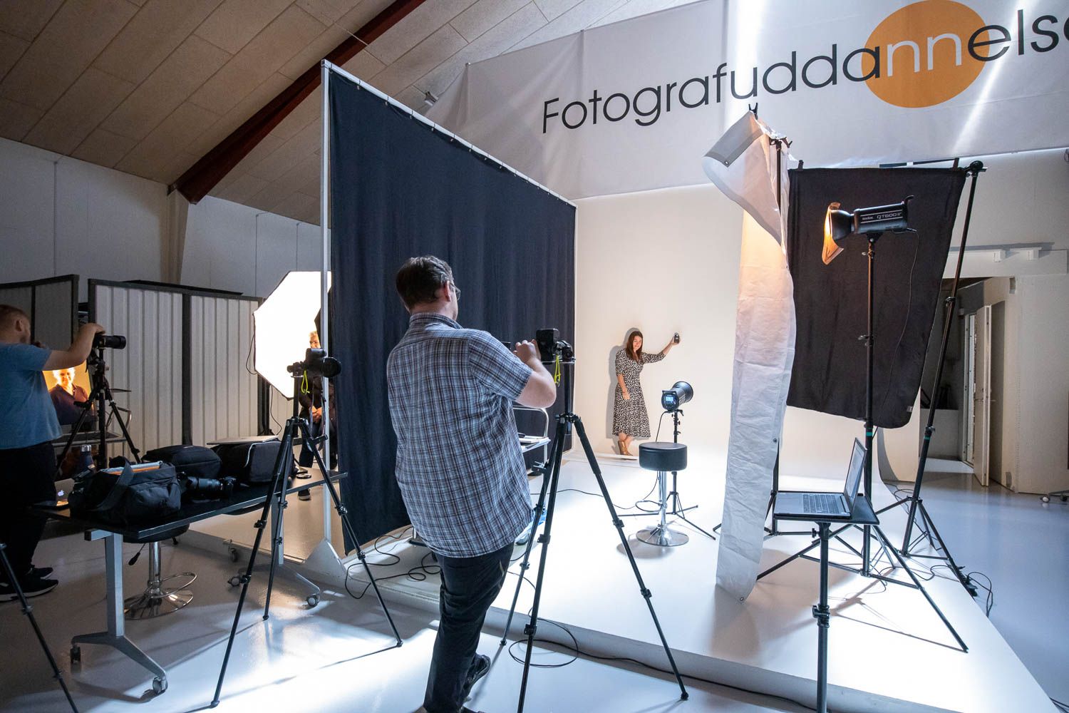 Wide angle view of a modern photography studio with lighting equipment and white backdrop setup.