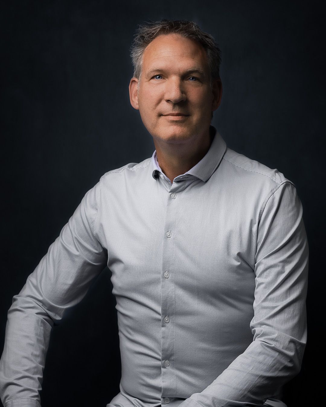 Professional studio portrait series in dramatic lighting showing man in white button-down shirt against dark background.