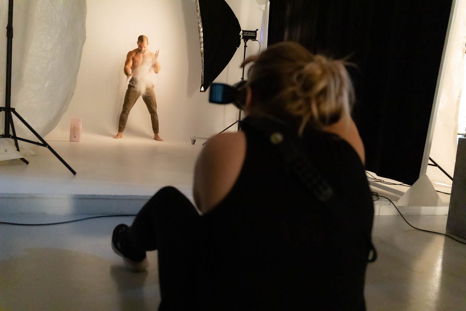 Photographer shooting against white backdrop in dark studio setting.