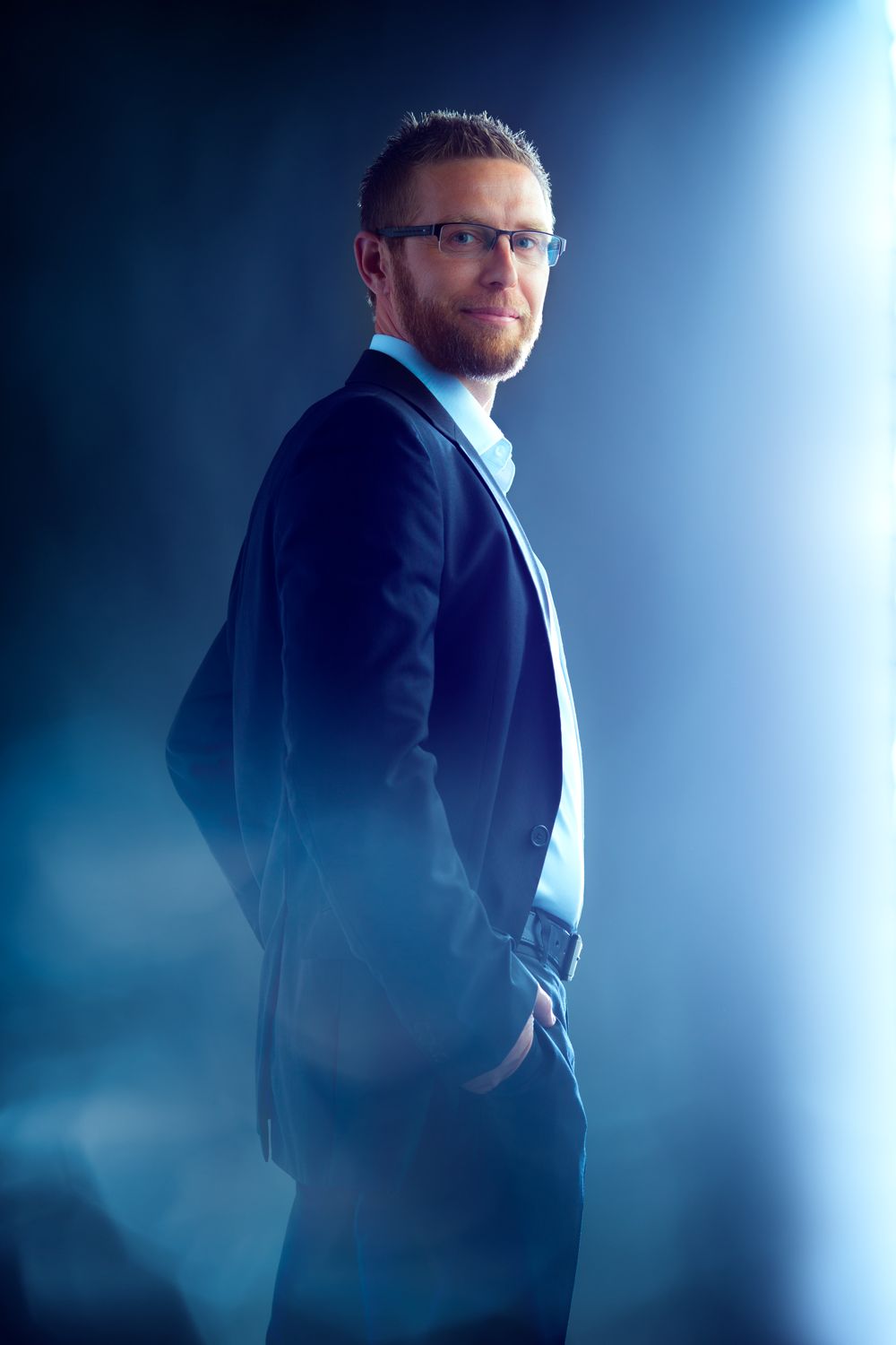 Professional business portraits with dramatic side lighting against blue background.