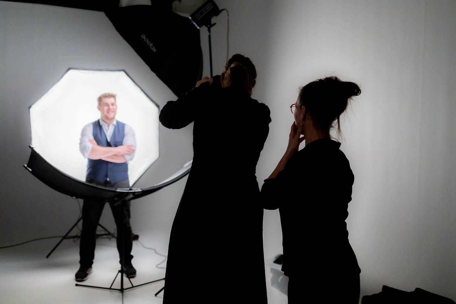 Behind the scenes silhouettes of photography team working in studio with lighting setup.