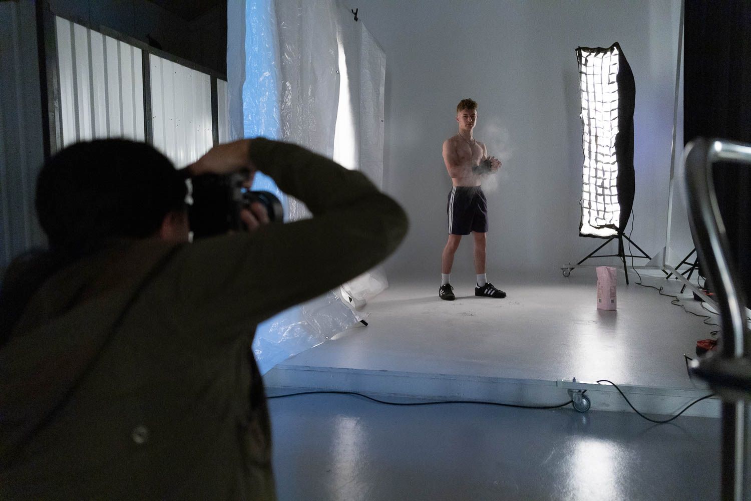 Photographer capturing fitness shoot in minimalist white studio with soft lighting.