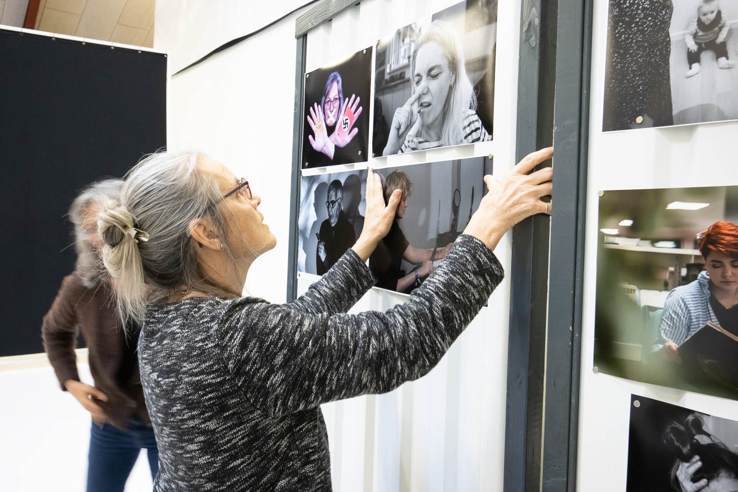 People examining photographs displayed on a white gallery wall during an exhibition.