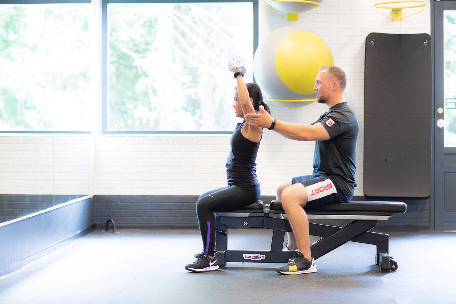 Personal trainer demonstrating proper form during an exercise session in a bright fitness studio.