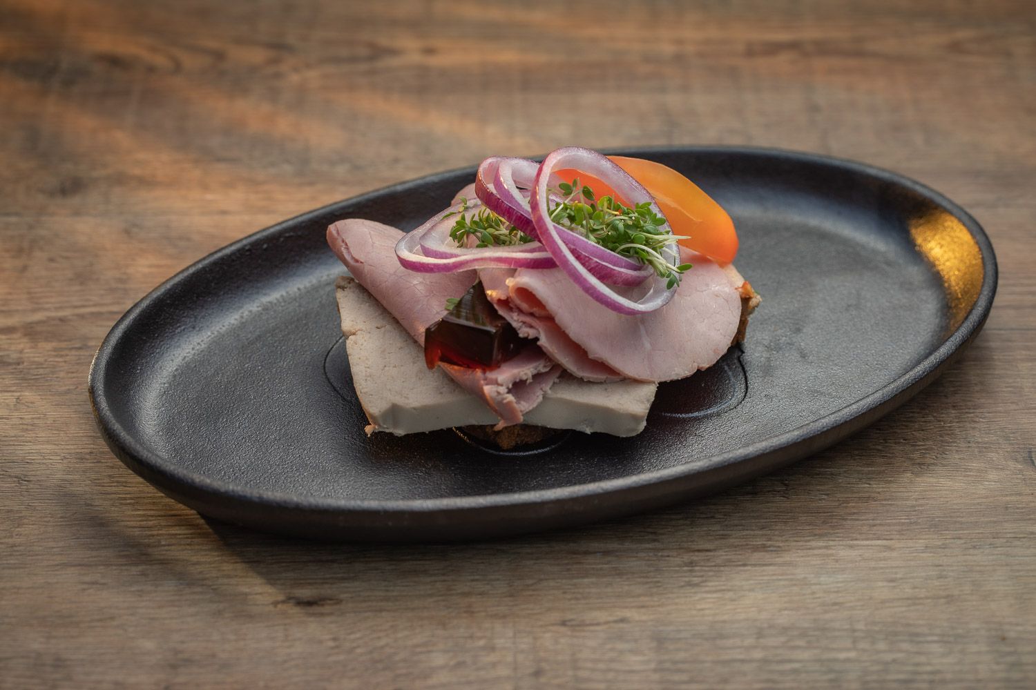 Thinly sliced meat appetizer garnished with fresh herbs on dark oval plate.