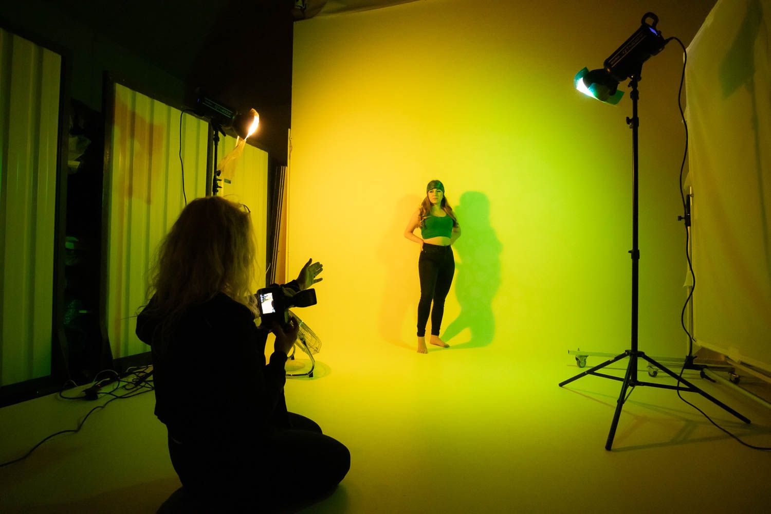 Photo shoot in progress with yellow-green lighting creating dramatic atmosphere in studio space.