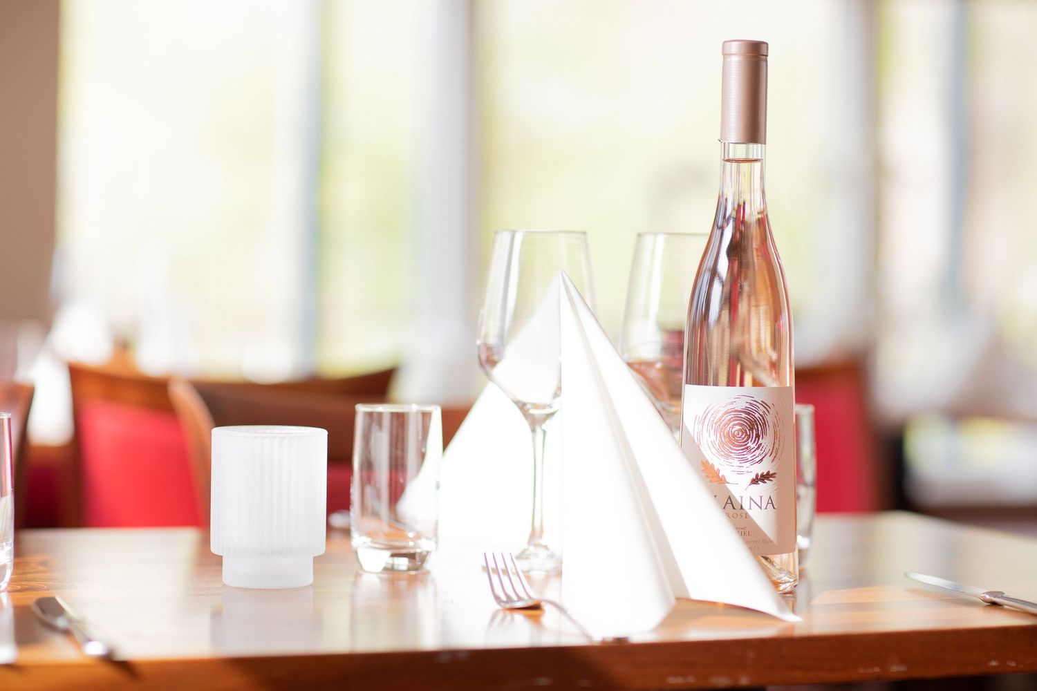 Rose wine bottle and glasses arranged on dining table with folded white napkins.