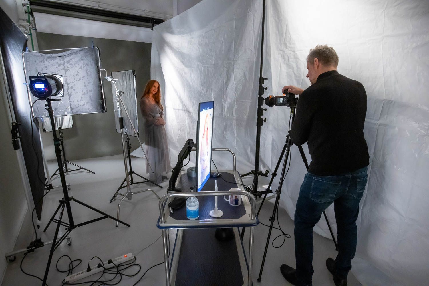 Photography studio setup showing various light stands and equipment against white walls.