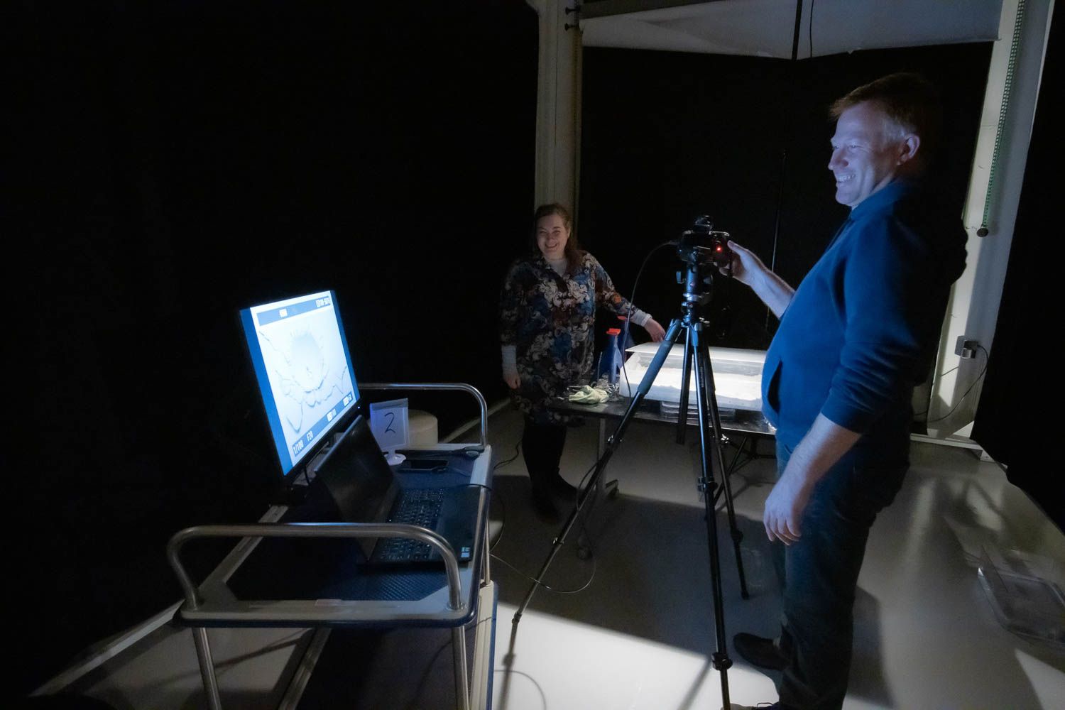Behind the scenes photo shoot setup with lighting equipment and white backdrop in professional studio.