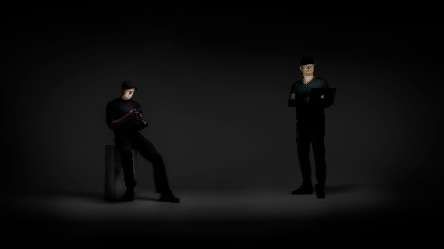 Silhouettes of standing figures arranged in dark dramatic lighting against black background.