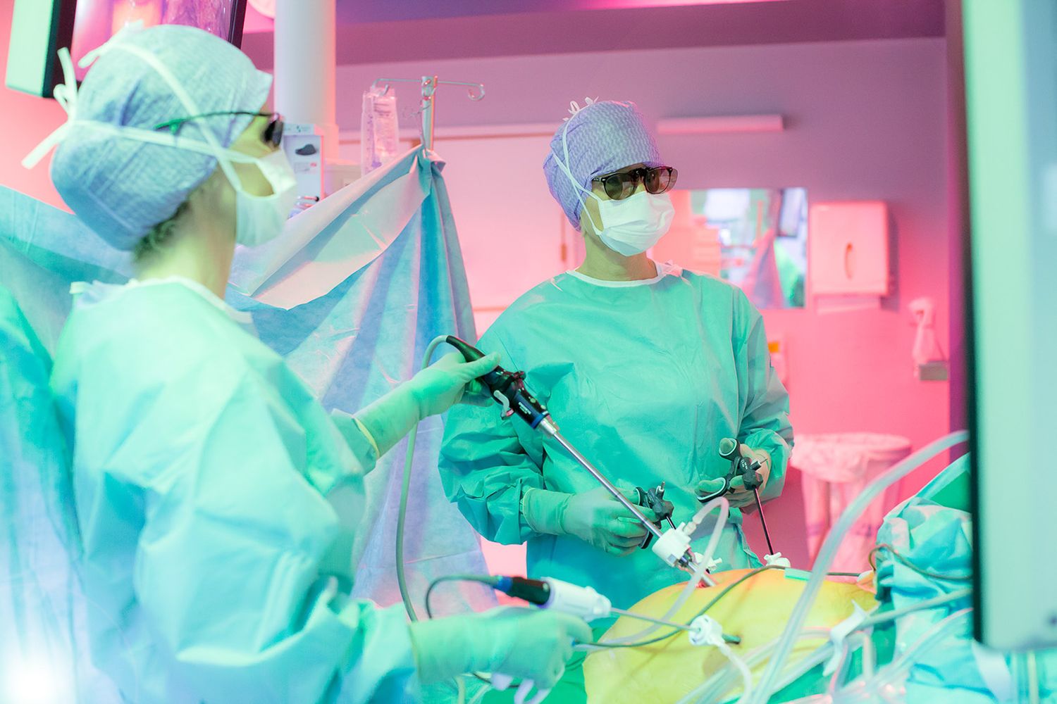 Operating room during surgical procedure with green and pink lighting.
