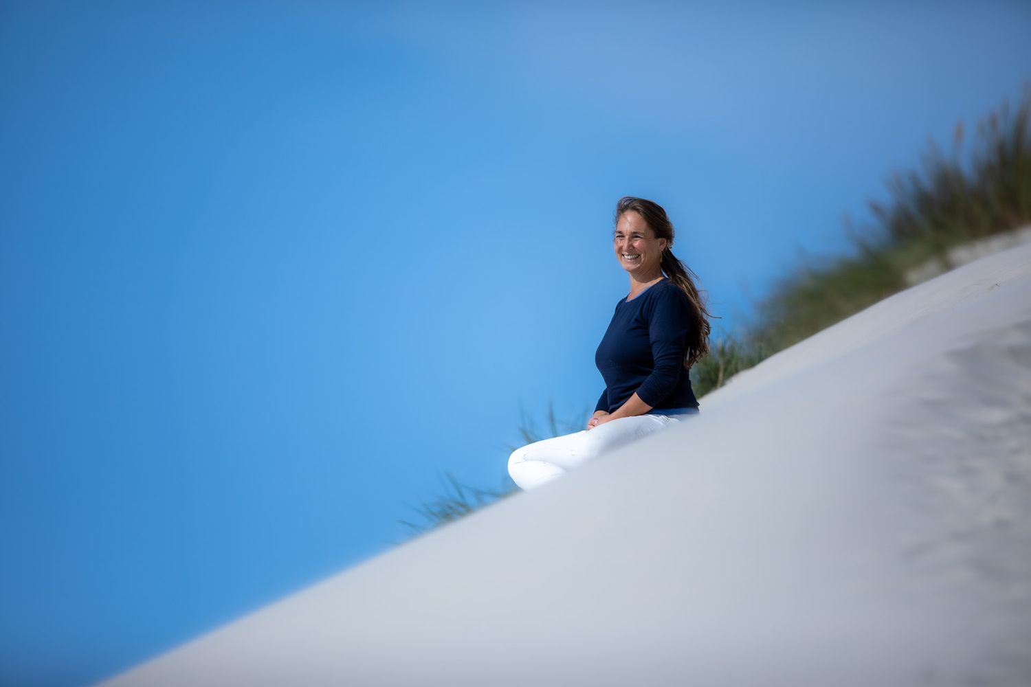 Playing fetch on a white sandy slope against bright blue sky.