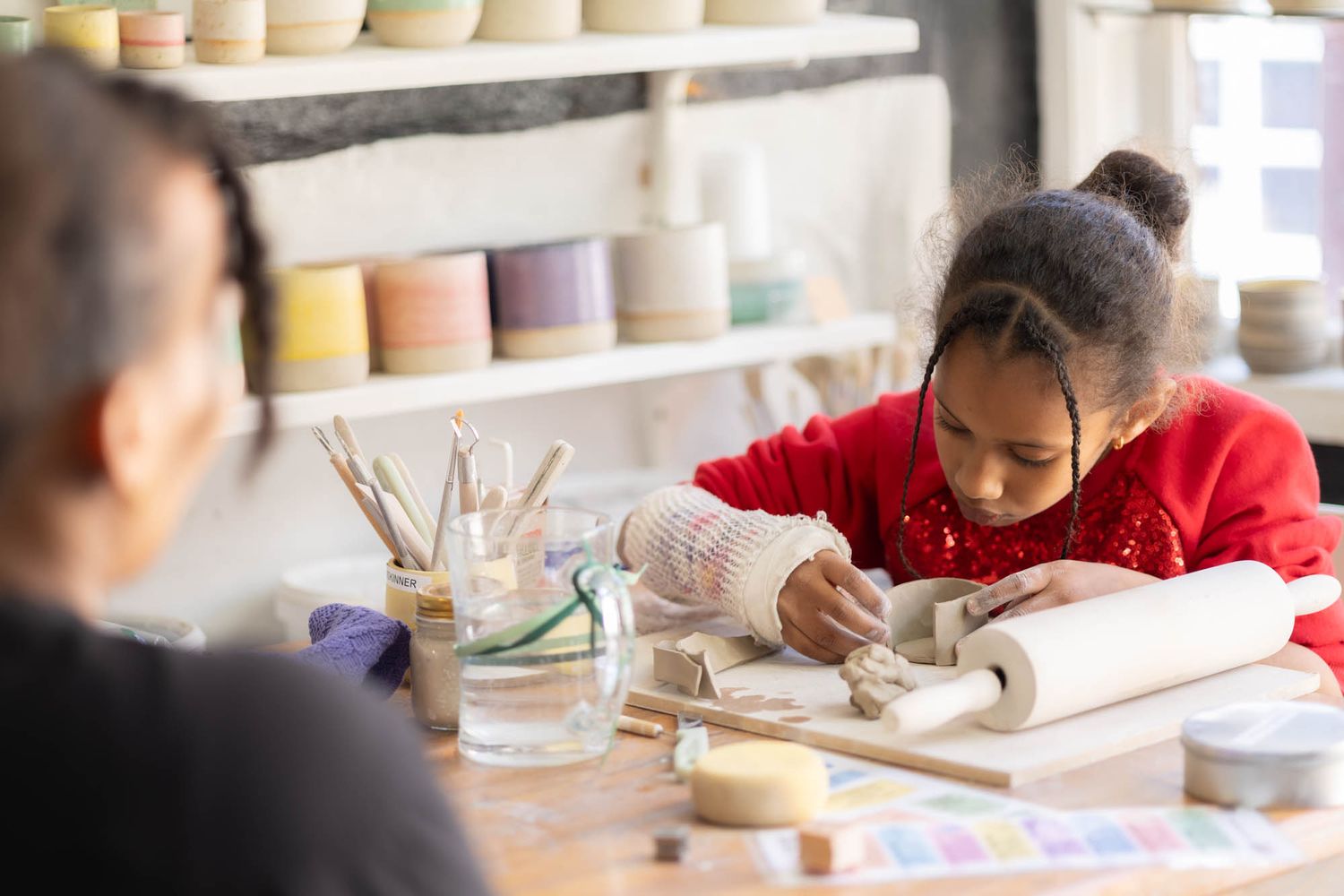Child working with clay at a pottery studio table with tools and supplies.