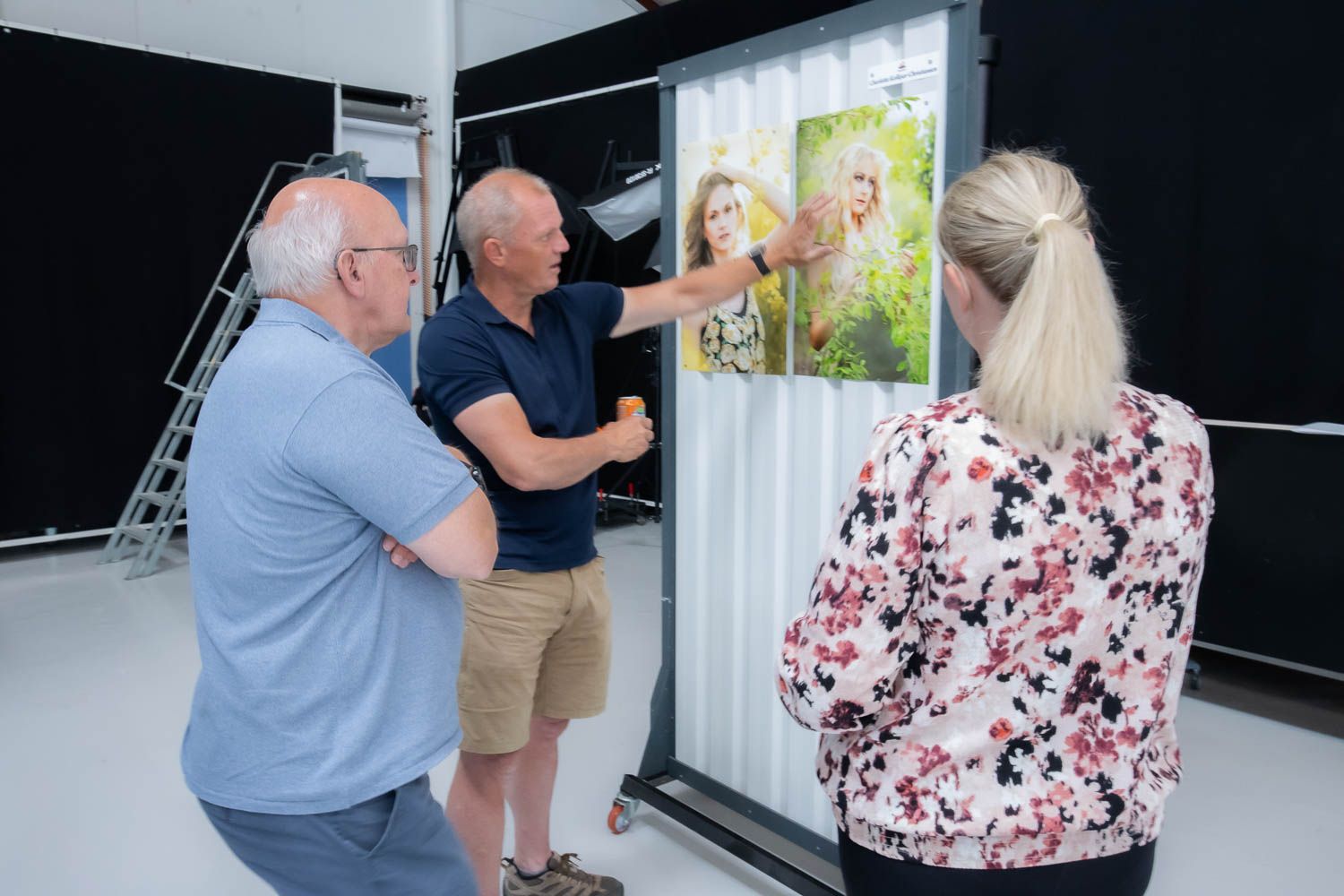 Three people examine and discuss prints displayed on a lightbox in a photography studio.