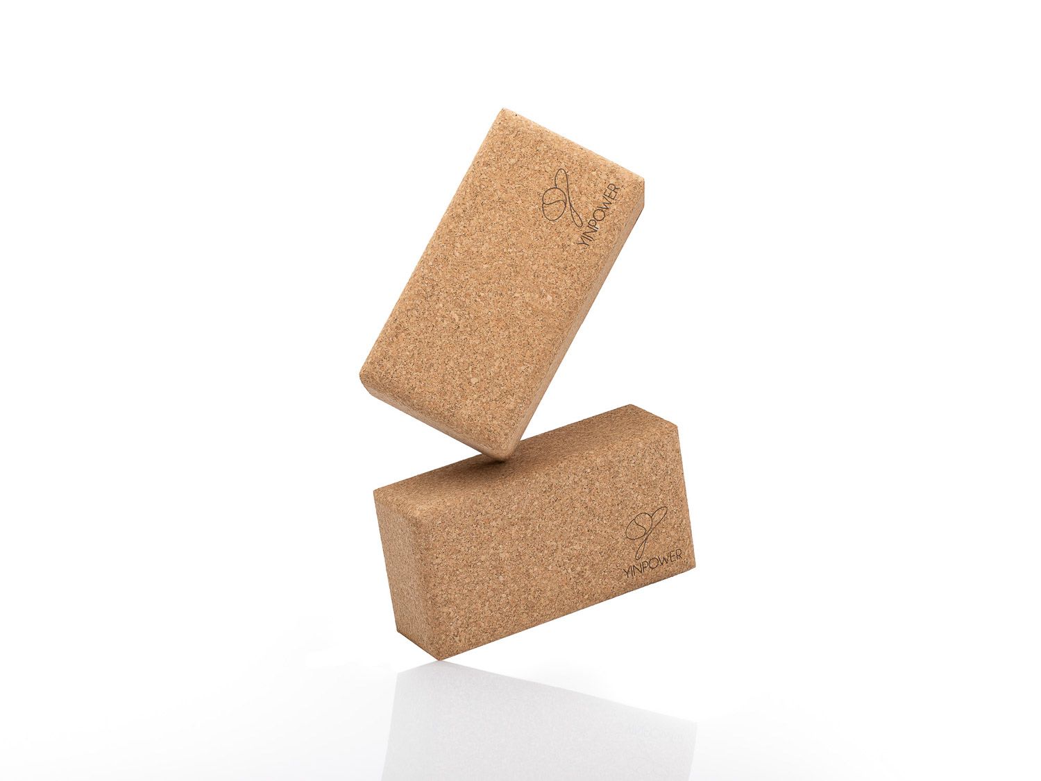 Cork yoga blocks balanced precariously against a white background demonstrating equilibrium.