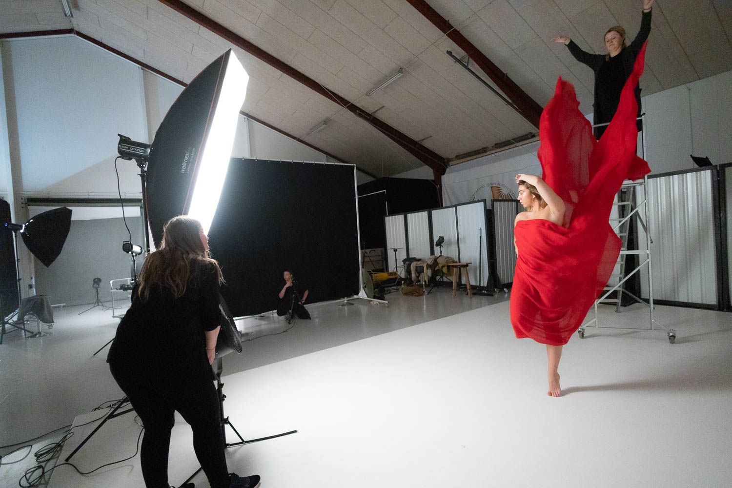 Photographer capturing dynamic movement of dancer in red dress against white studio backdrop.