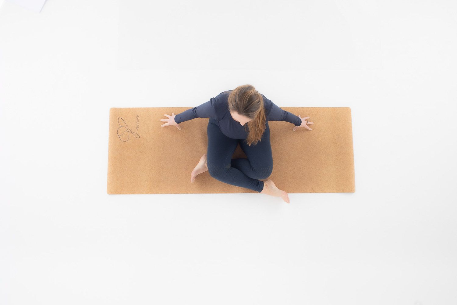 Overhead view of person practicing yoga on cork mat against white background.