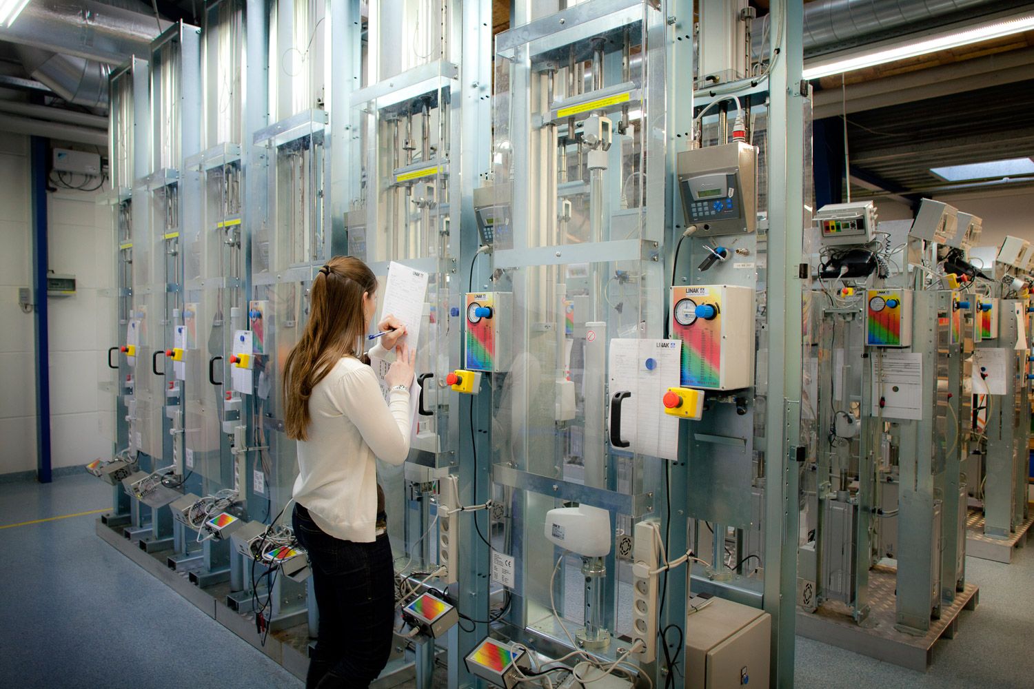 Researcher examining industrial laboratory equipment in facility hallway.