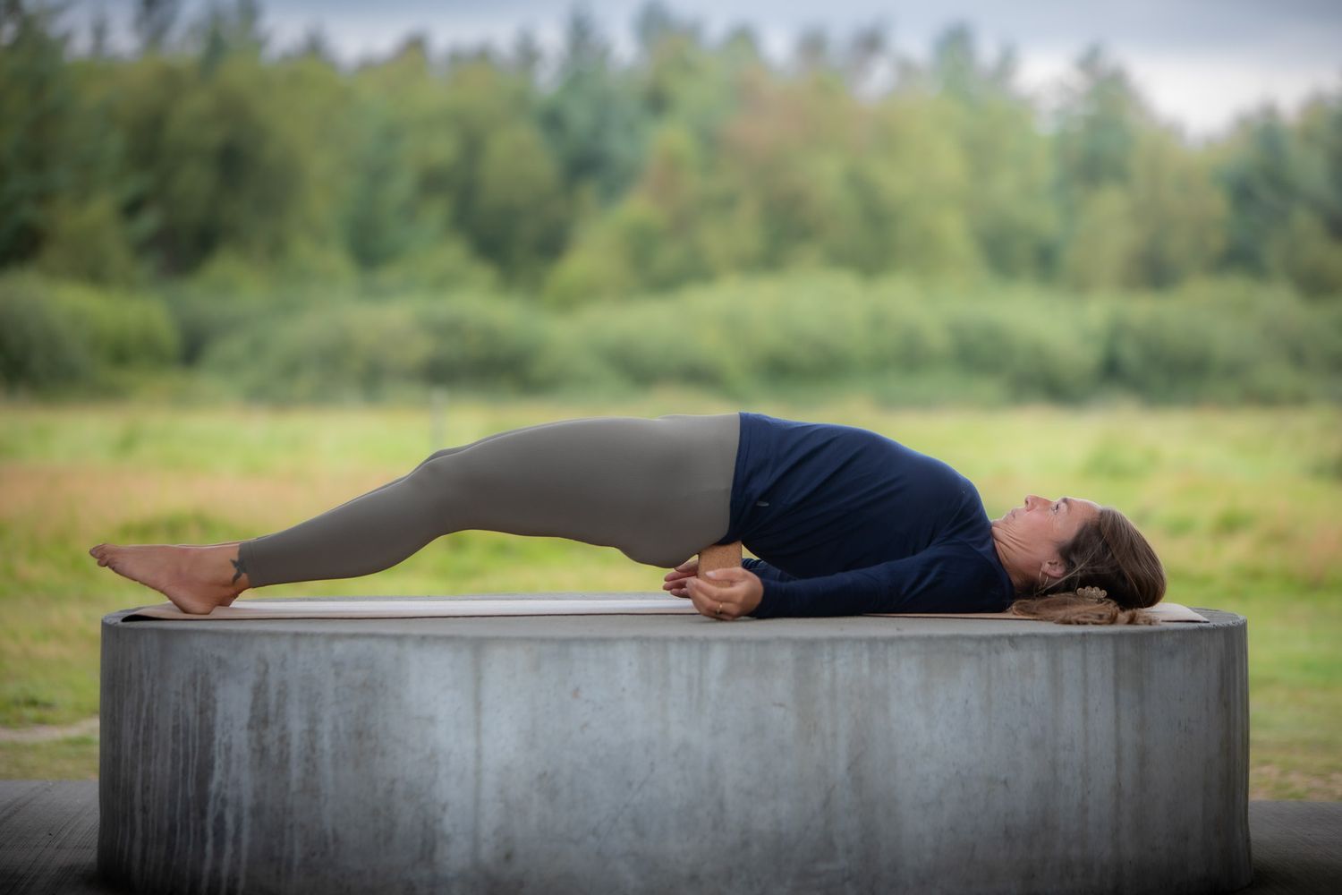 Person demonstrating restorative yoga pose on concrete platform in nature.