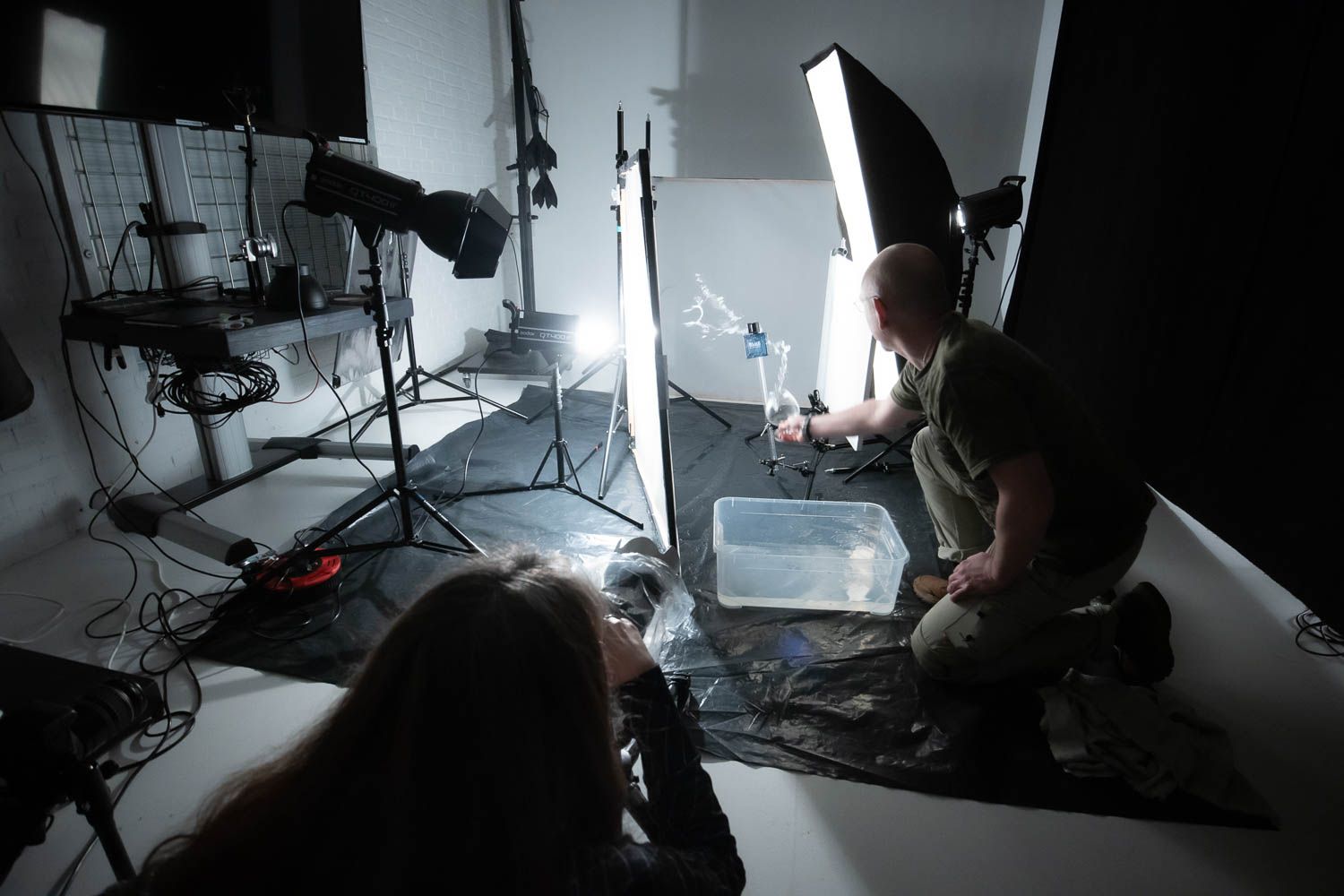 Behind-the-scenes view of a dark photography studio with lighting equipment and camera setup.