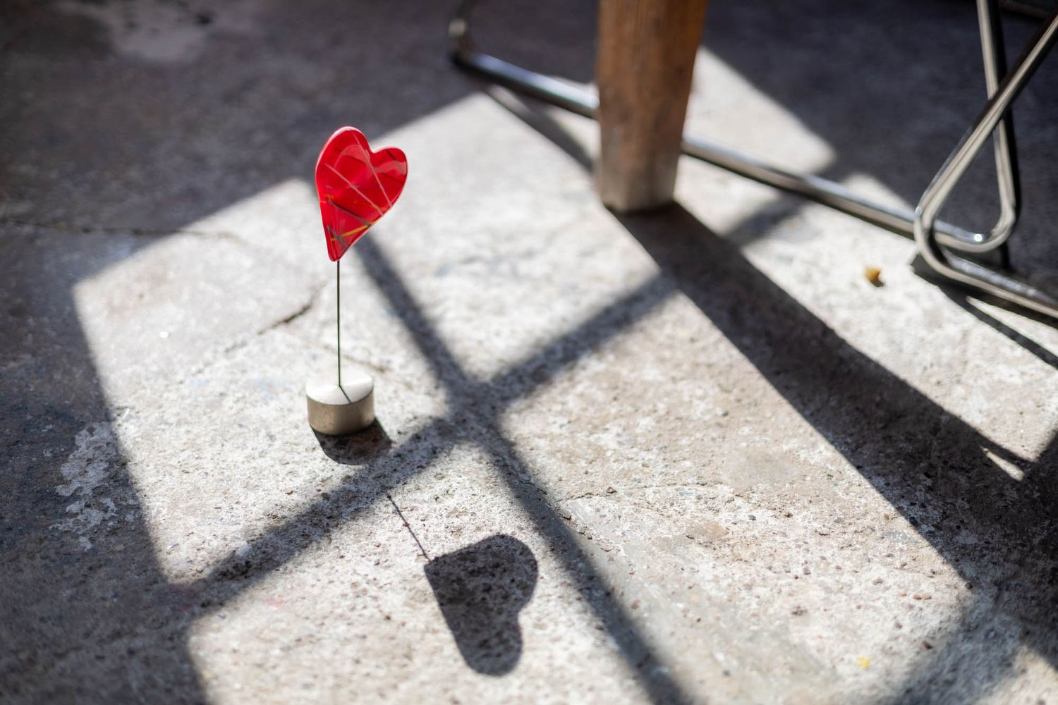 Small red heart decoration casting shadow on concrete floor in sunlight.