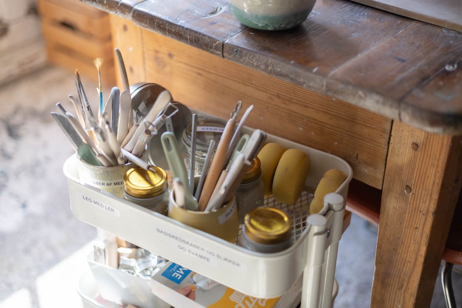 Ceramic pottery and utensils displayed on wooden shelving in a craft studio.