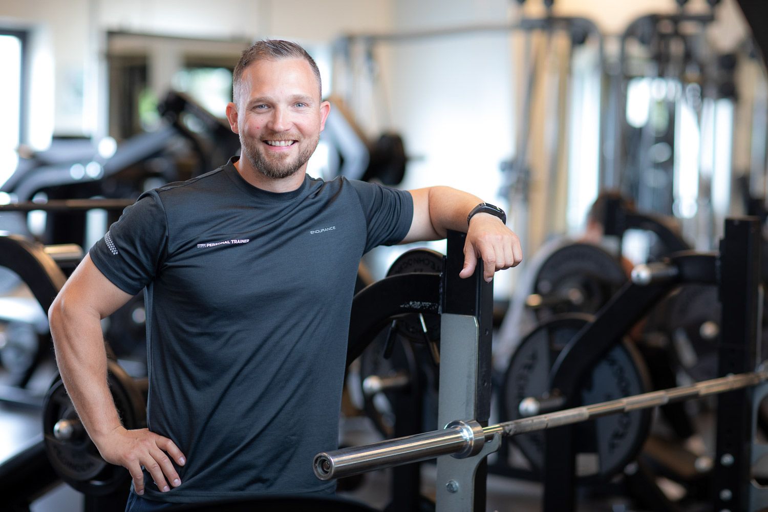 Athletic trainer in dark workout attire positioned in well-equipped gym space.