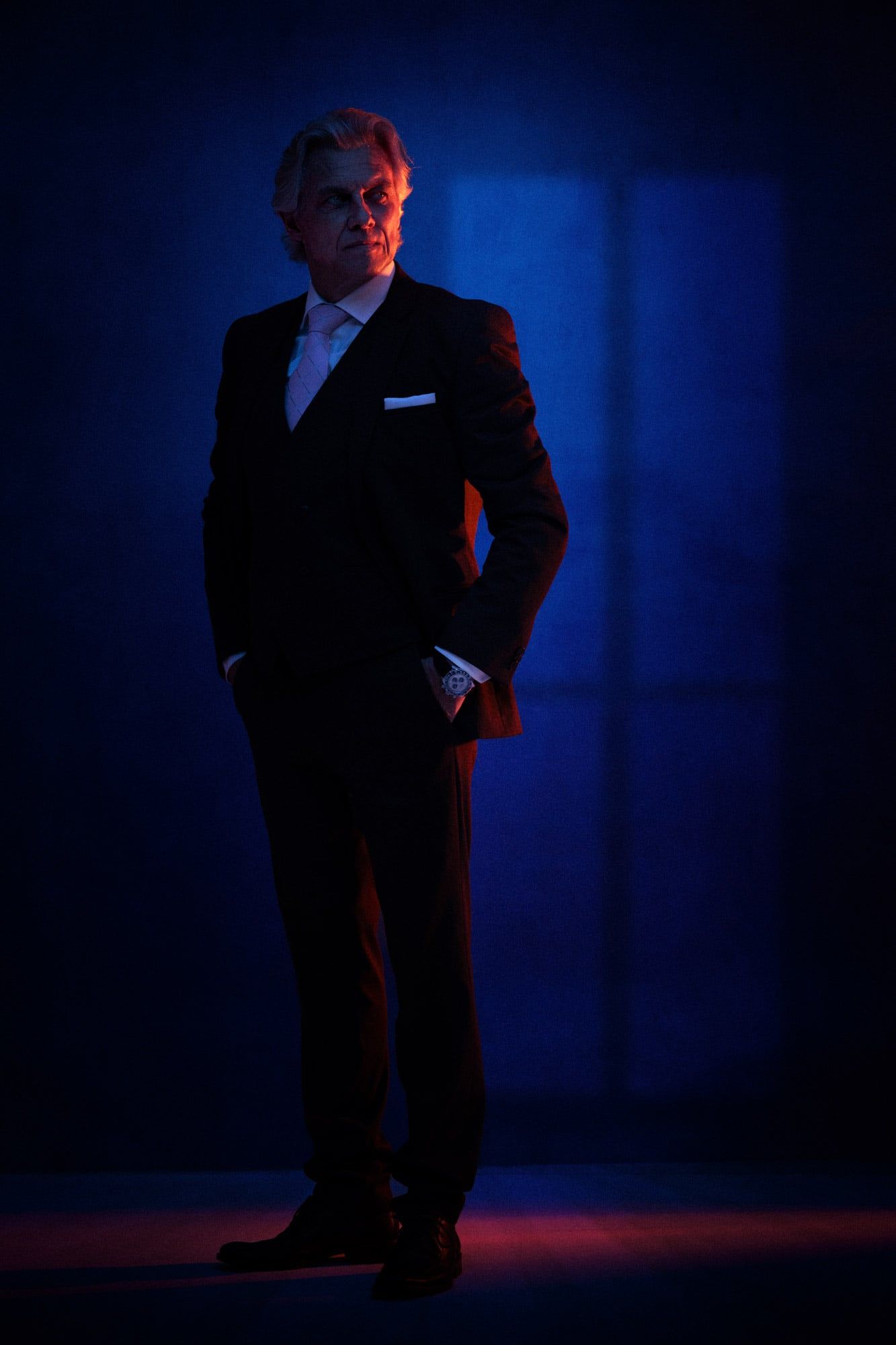 Moody business portrait series with figure in dark suit illuminated by blue studio lighting.