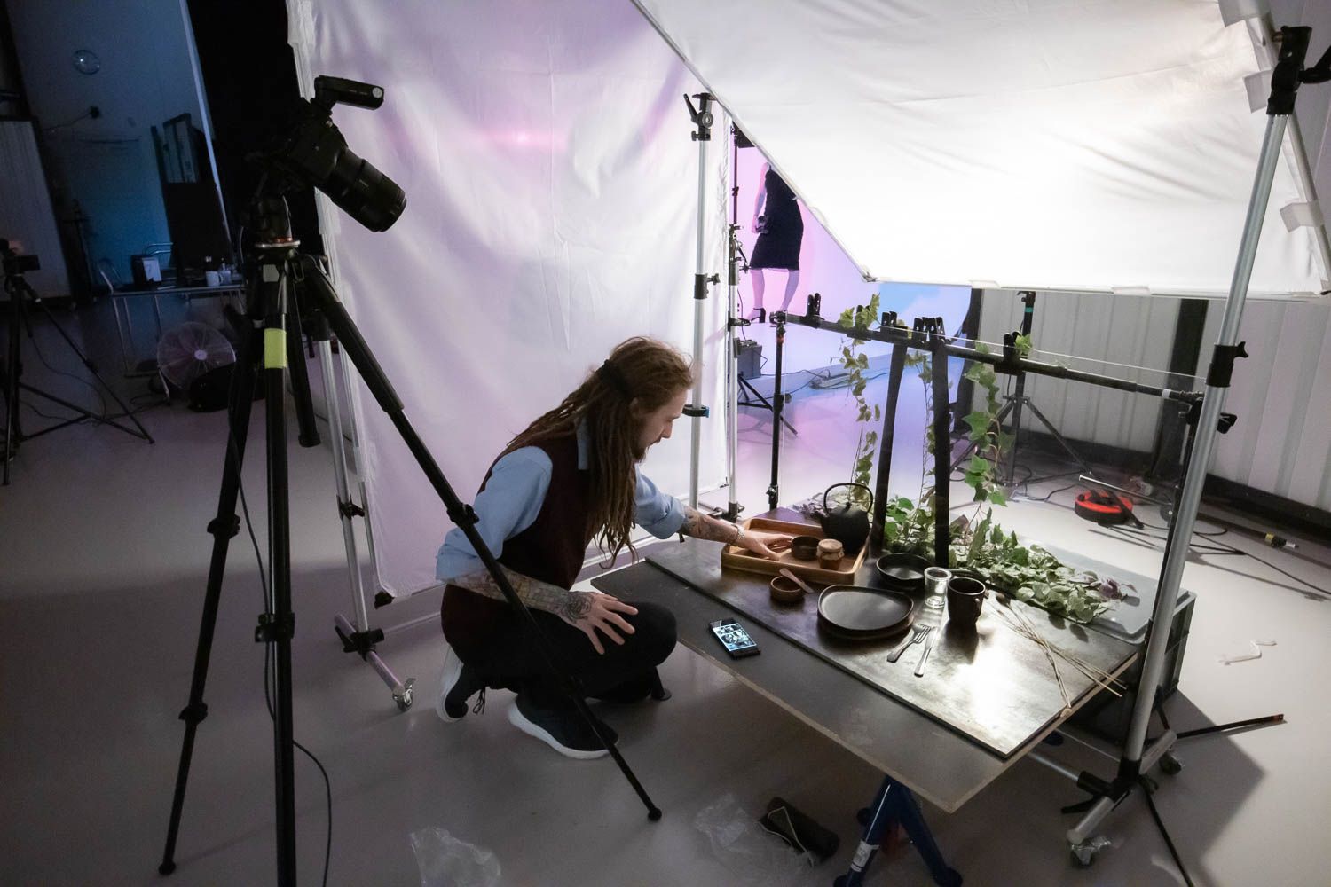 Photographer setting up detailed product photography with plants and props in studio environment.