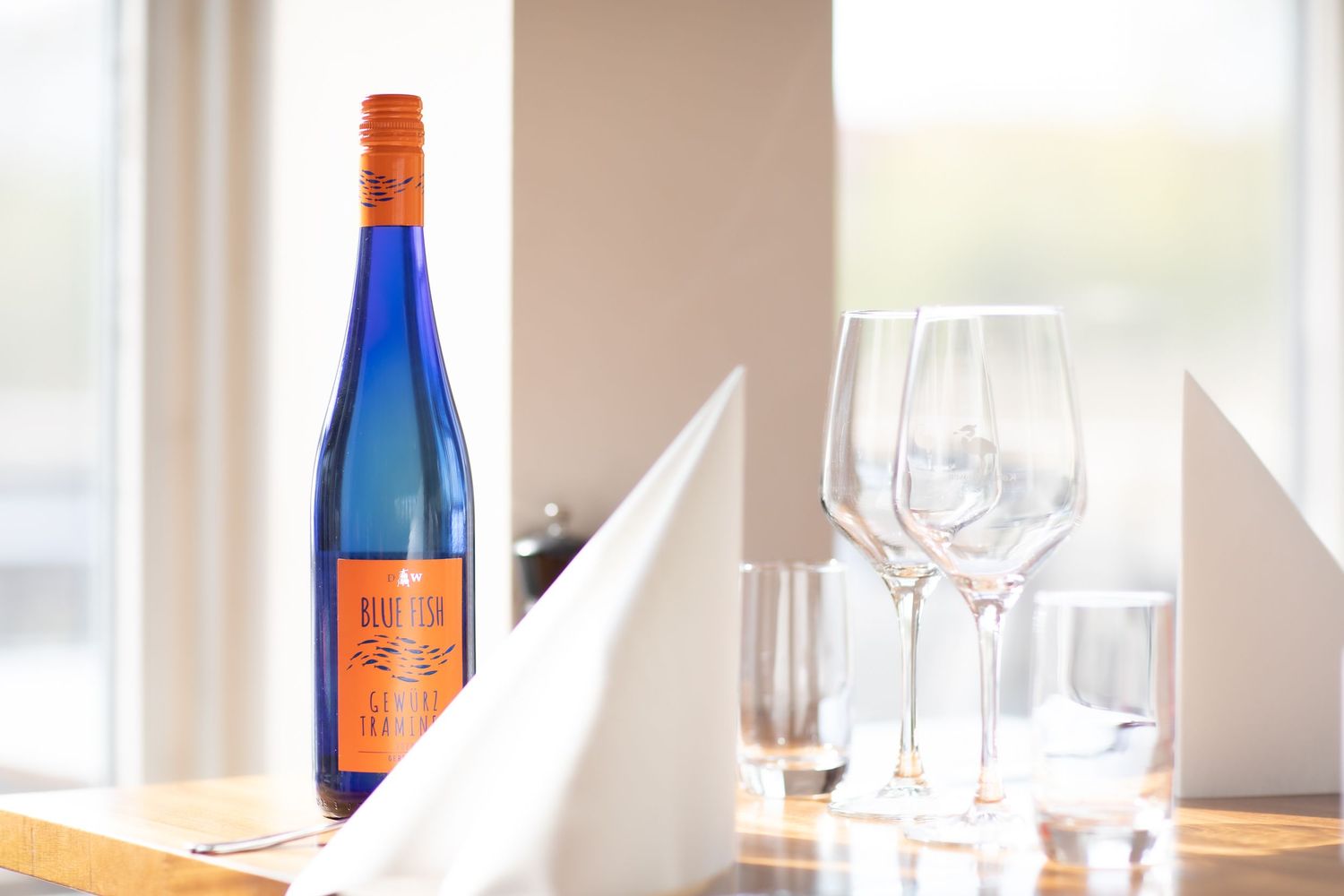 Blue wine bottle and empty wine glasses set on elegant white tablecloth in natural lighting.