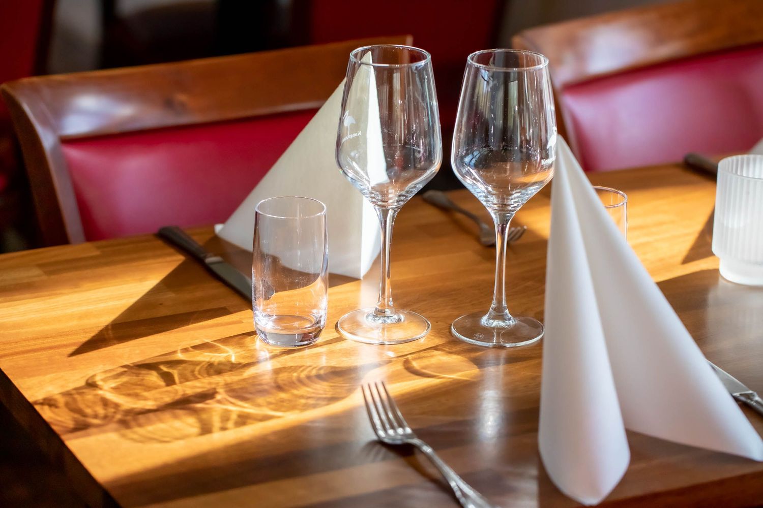 Elegant table setting with wine glasses and white napkin on wooden restaurant table.