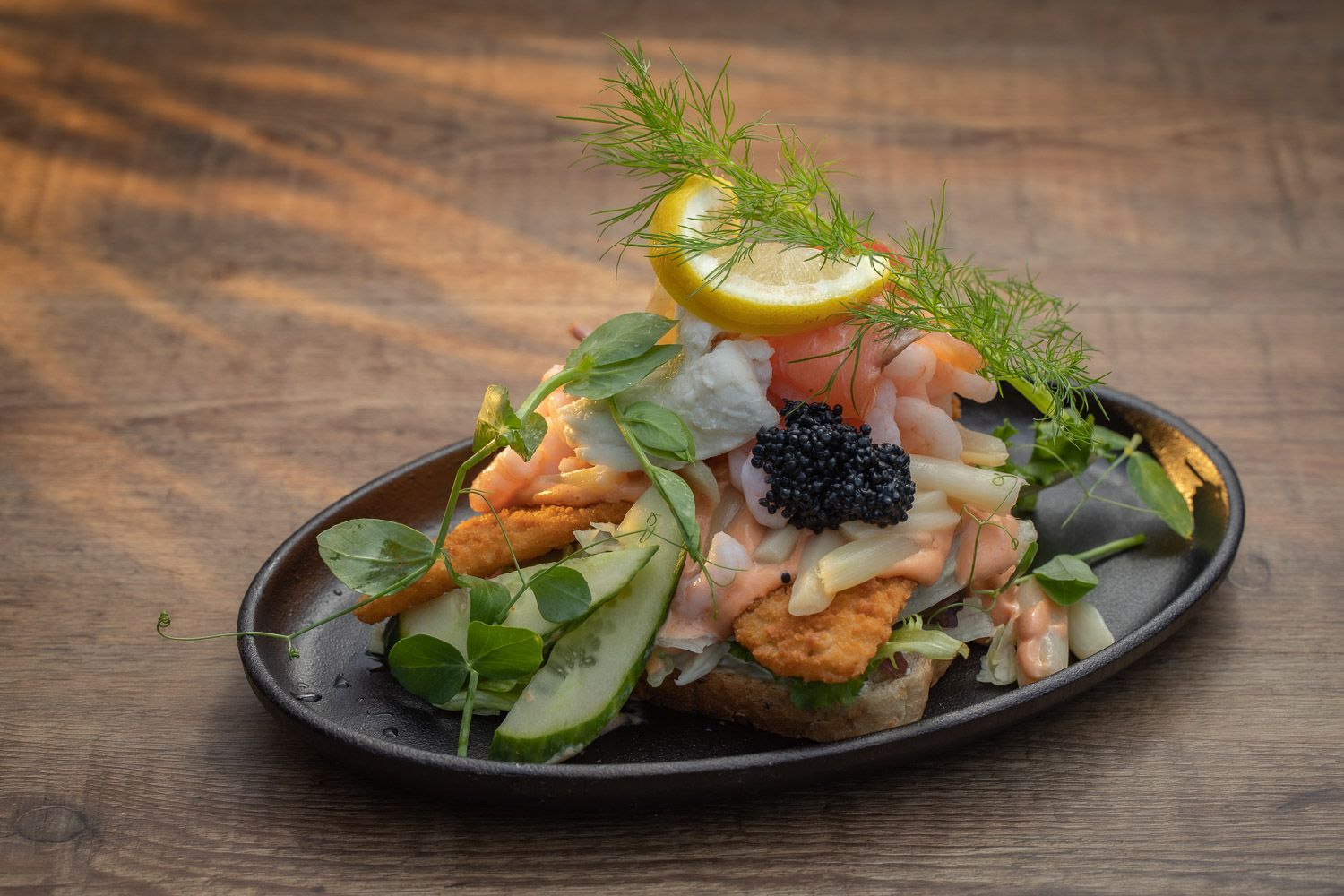 Elegant seafood appetizer with salmon, caviar and fresh herbs on black plate.
