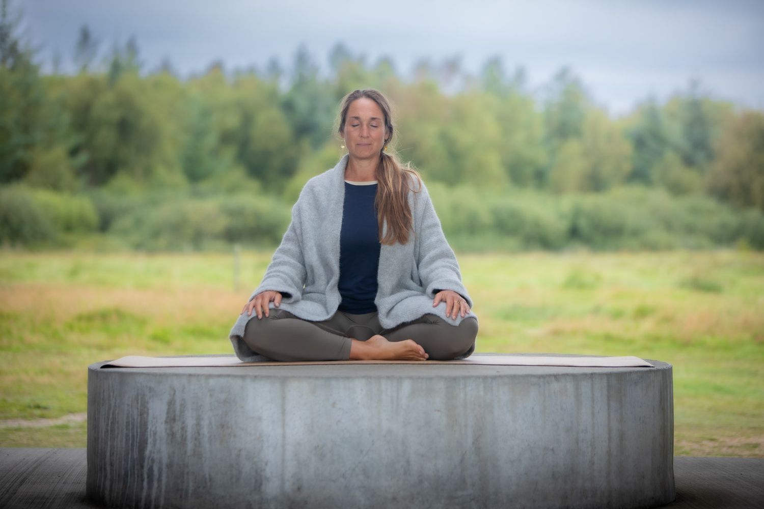 Person meditating in lotus position on concrete platform with nature background.
