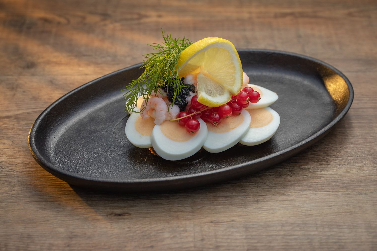 Elegant appetizer plate with sliced eggs, garnish, and lemon on black dinnerware.