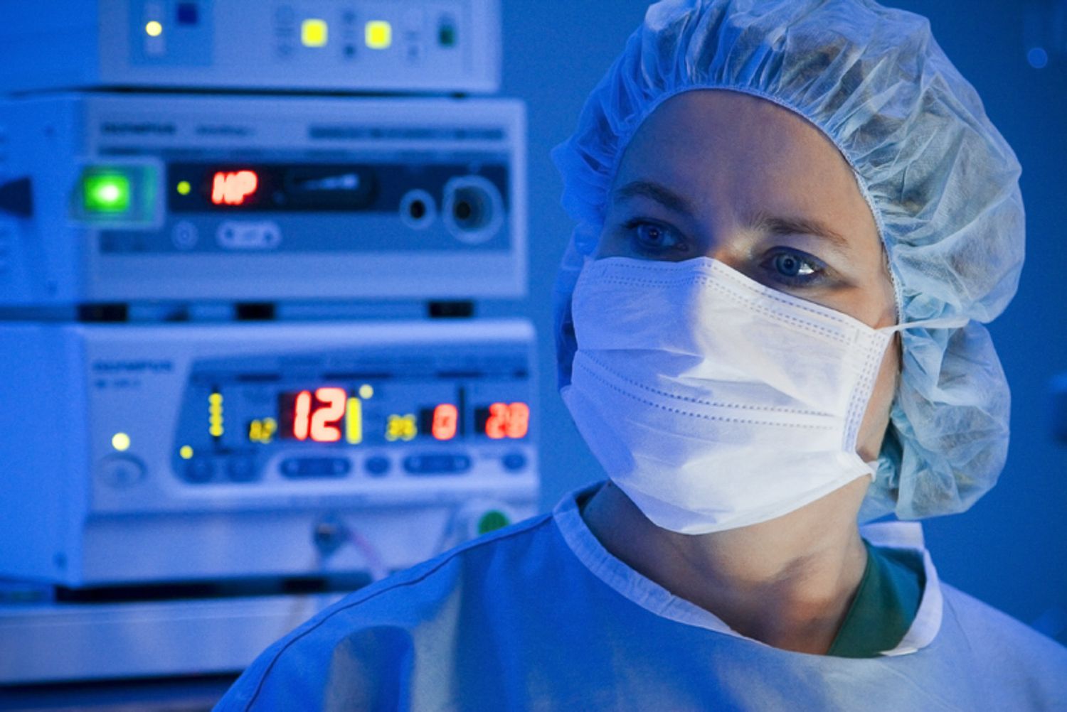 Surgical team wearing protective gear working in modern operating theater with blue ambient lighting.