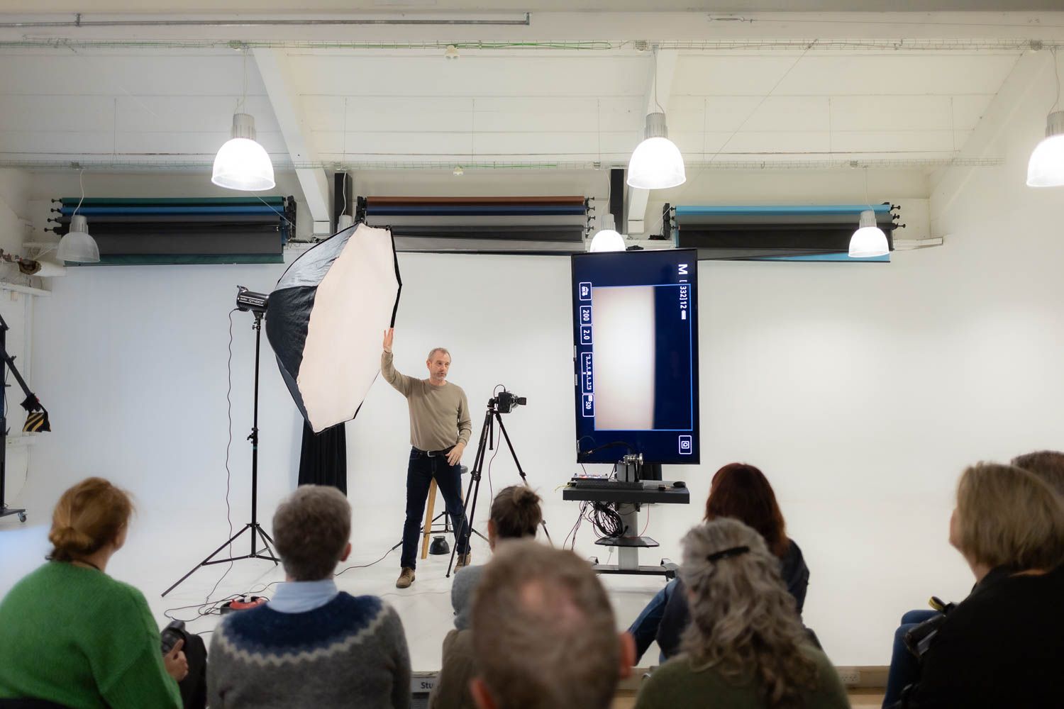 Photography students learn lighting techniques in a bright studio classroom setting.