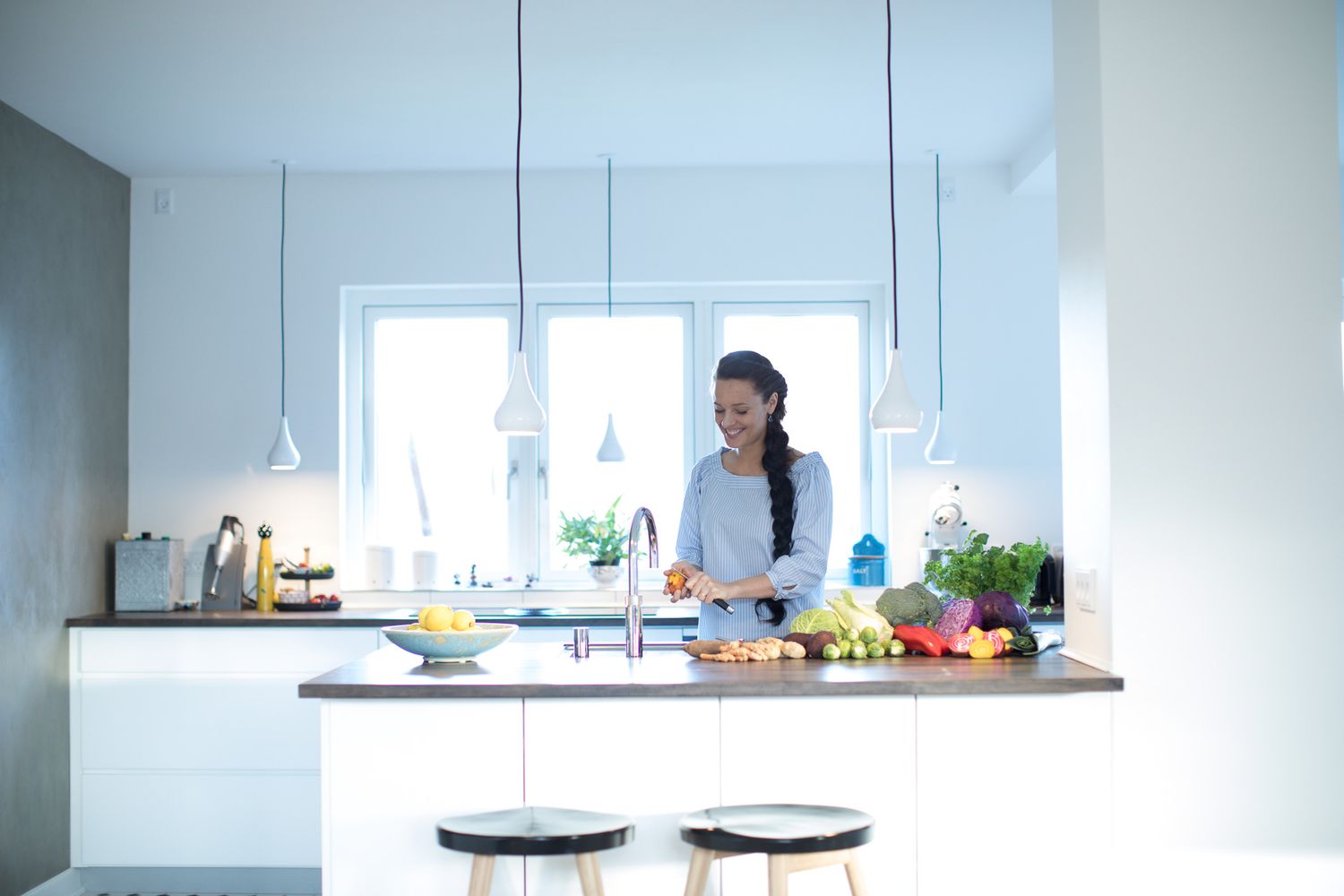 Modern kitchen interior with pendant lights and white countertops featuring fresh ingredients and cooking preparation.