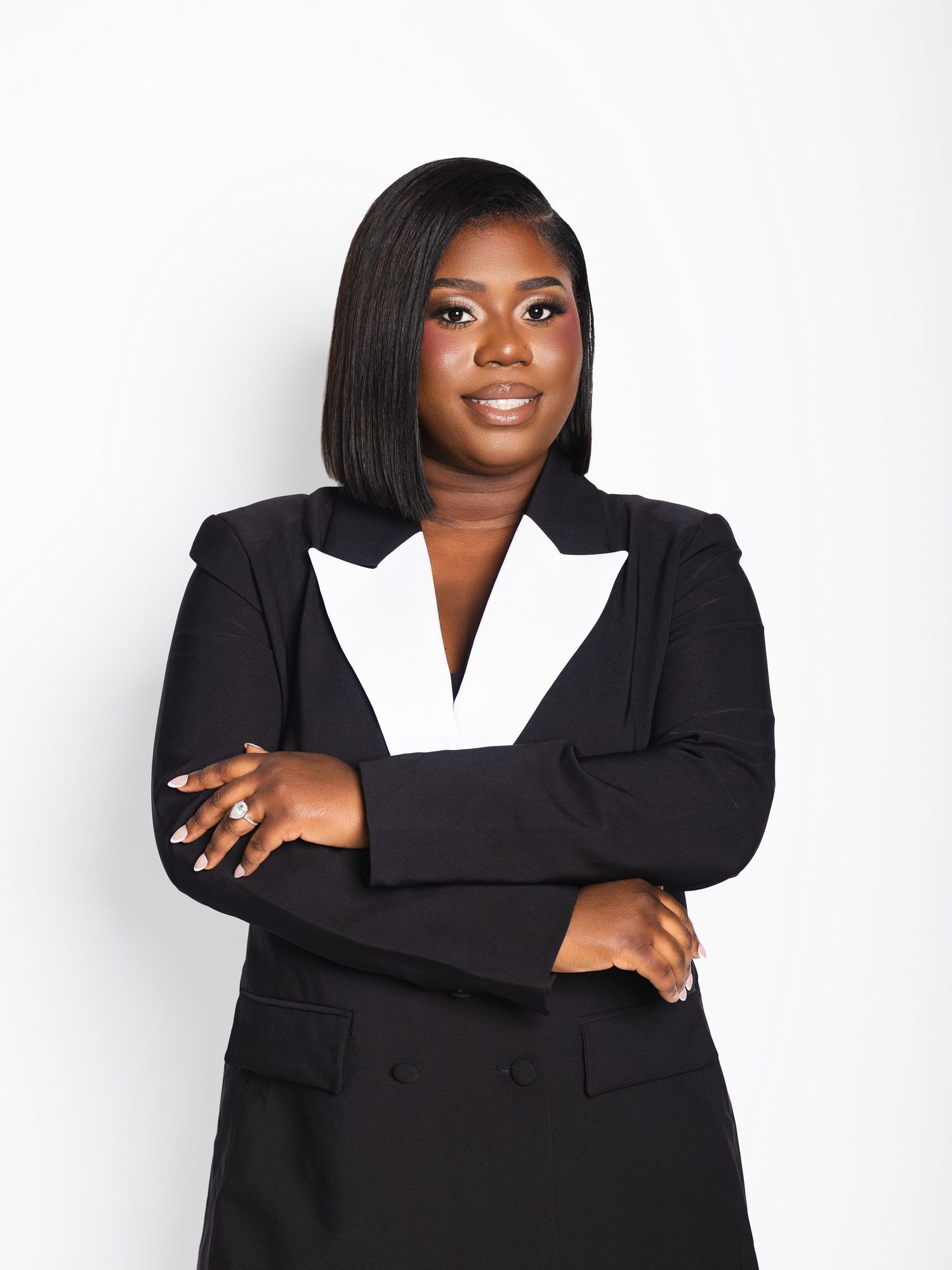 Confident woman in black double-breasted blazer with white lapels posing with arms crossed on white background.